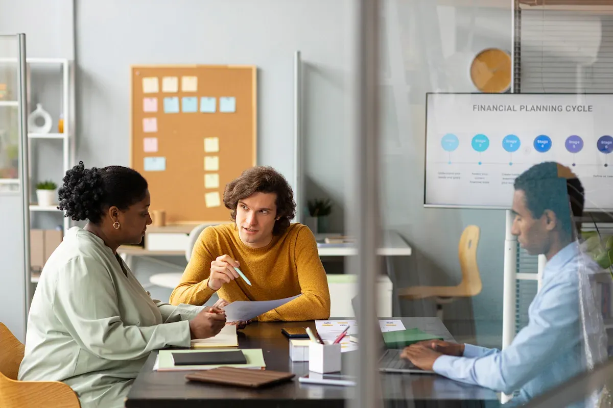 Top of image is 3 people talking in a meeting in a non-profit office.