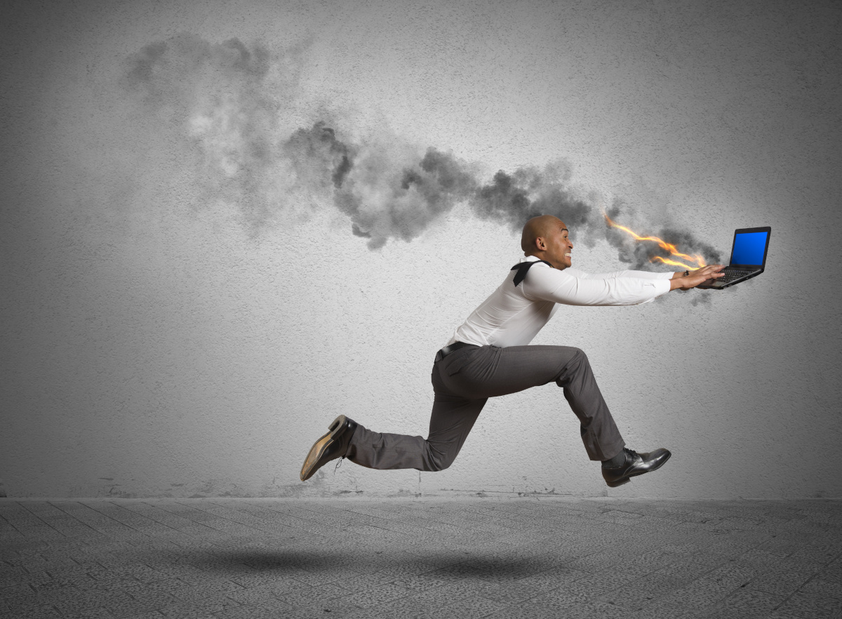 Man in business attire running while typing on a flaming laptop that is leaving a smoke trail