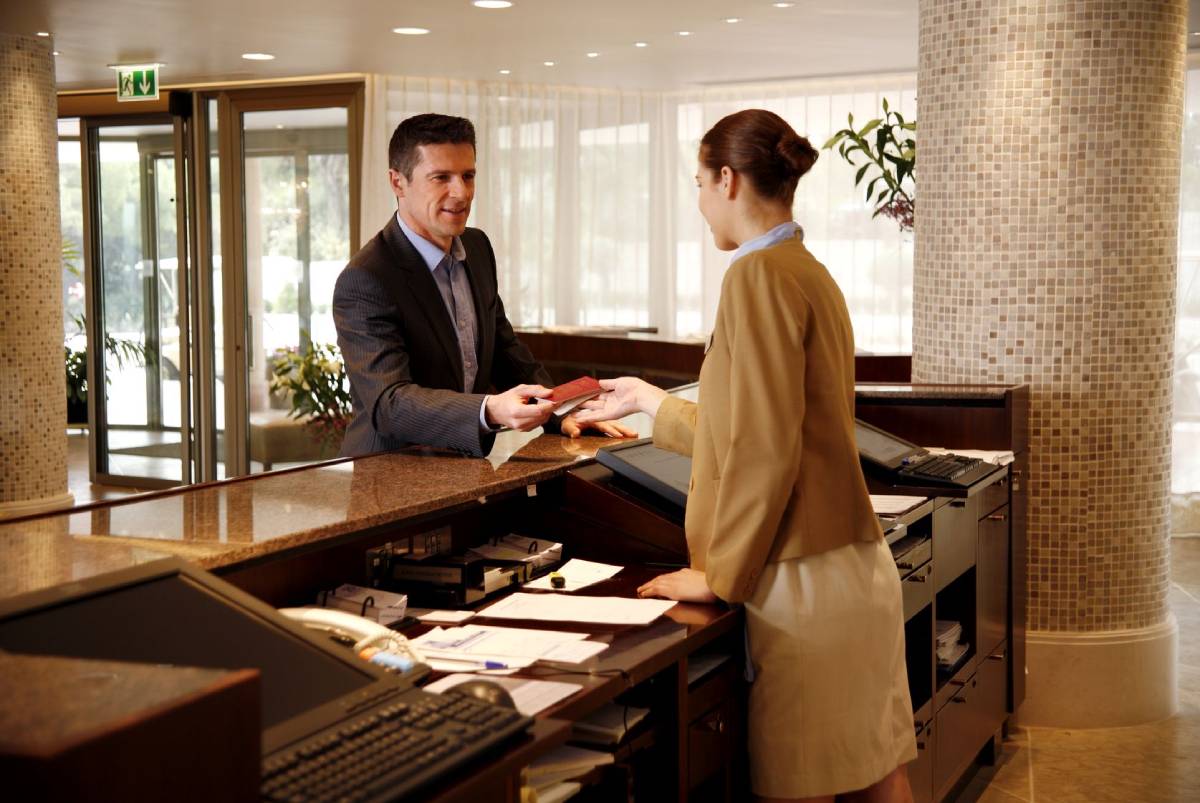 A female hotel employee helping a businessman check in.