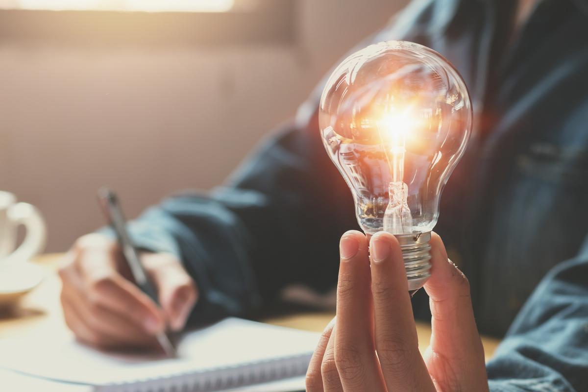 Man holding a lightbulb while working on laptop