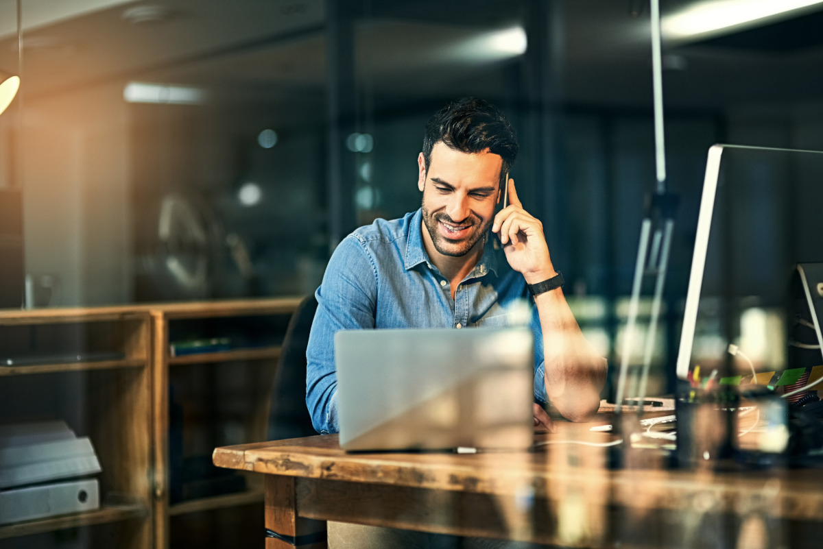 A man talking on his phone while looking at a laptop in his business office