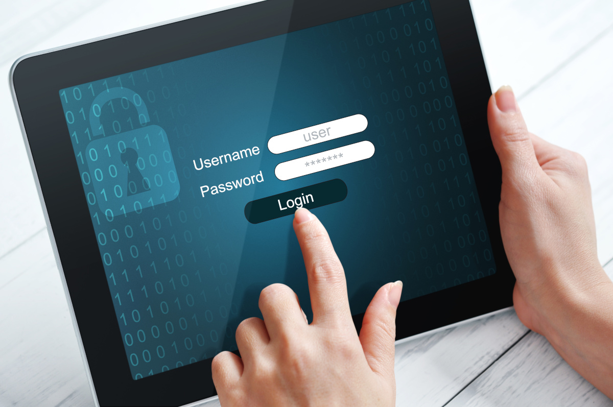 Close up of hands using tablet with username and password login prompt on screen.