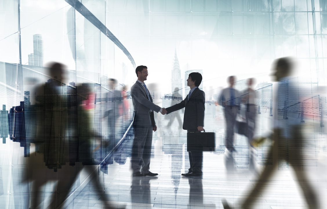 Two businessmen shaking hands, with other business people in the background