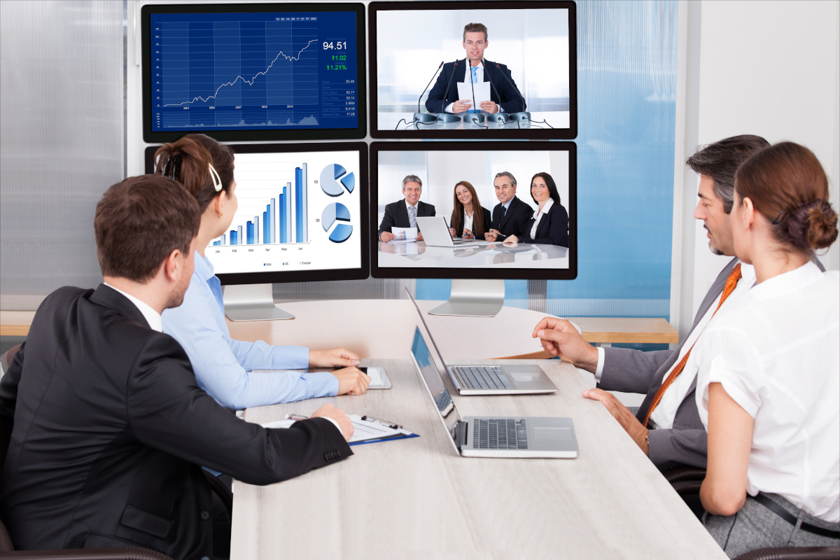 Four business people looking at four monitors showing graphs