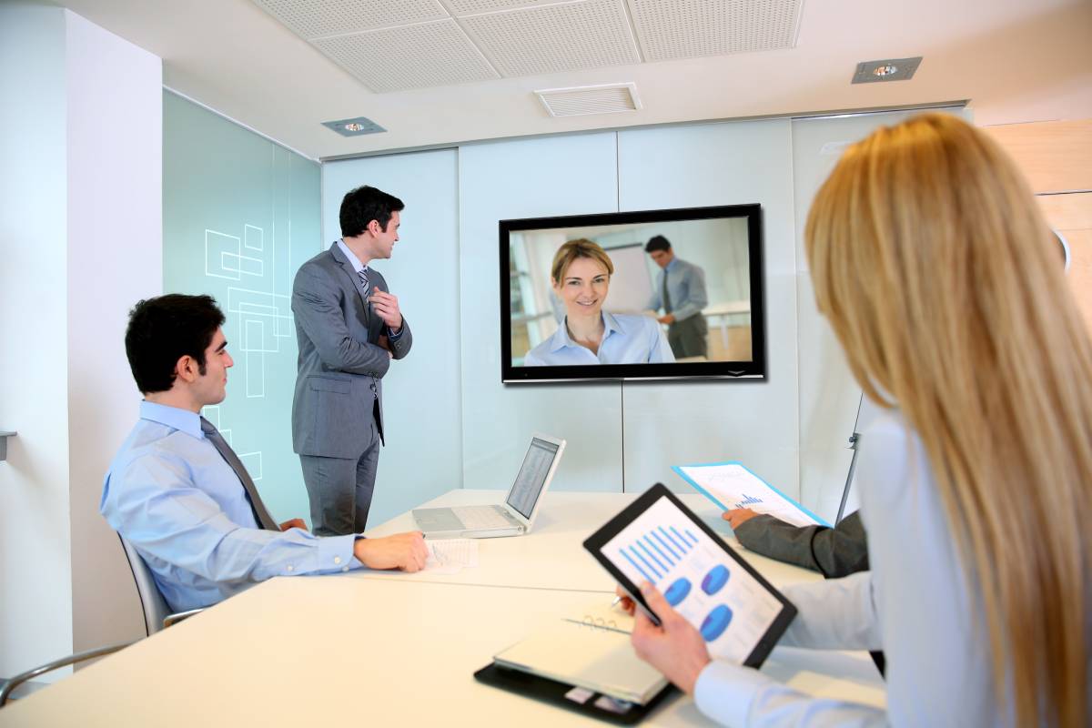 Two businessmen and a businesswoman using video conferencing technology to speak with a businesswoman.