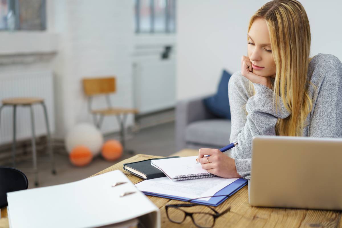 A blonde woman working remotely doing paperwork at her desk